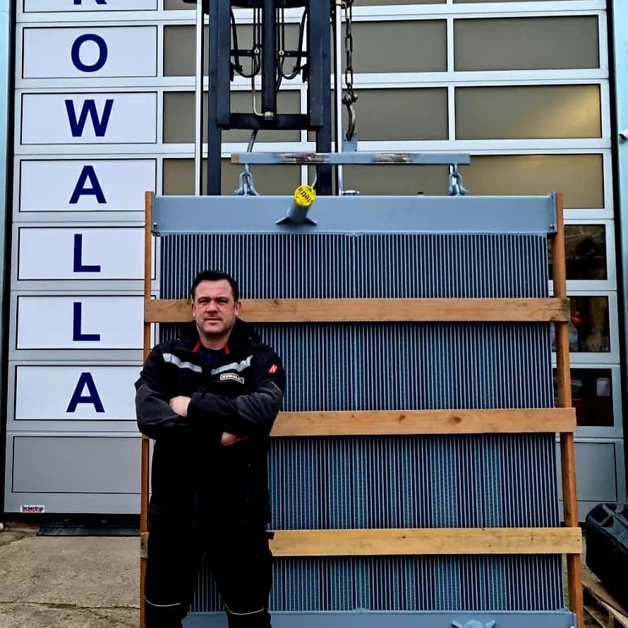 Tim Kowalla steht mit verschränkten Armen vor einem großen Industriekühler vor seiner Werkstatt
